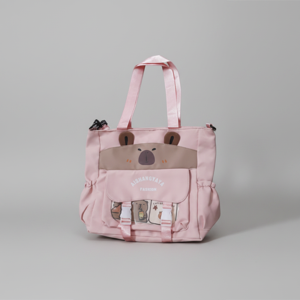 A pink tote bag with a cute cartoon bear face on the front pocket and a flap pocket featuring cartoon characters. The bag has pink shoulder straps and a zip-top closure, with the brand name 'NISHANGAYA FASHION' printed on the front pocket.